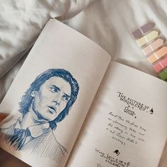 an open book with a drawing of a man's face on the page and colored crayons next to it