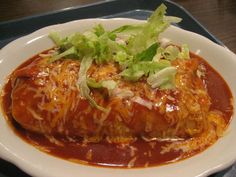 a white plate topped with meat covered in sauce and garnished with lettuce