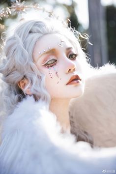 a close up of a person with white hair and makeup wearing an angel wings outfit