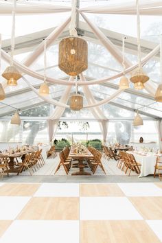 the inside of a tent with tables, chairs and chandeliers hanging from the ceiling