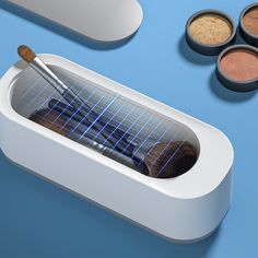 an assortment of makeup products on a blue surface with one brush in the container and four eyeshades next to it