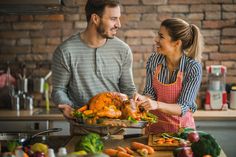 a man and woman standing in front of a turkey on a platter with vegetables