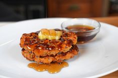 a white plate topped with pancakes covered in syrup next to a small bowl of honey