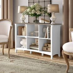 a white bookcase with flowers and books on it in front of a mirror next to two chairs