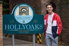 a man standing in front of a welcome sign for hollyoaks village, california