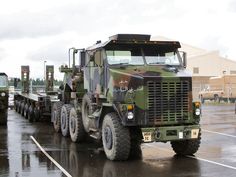 an army truck is parked in a parking lot with other trucks behind it on a rainy day