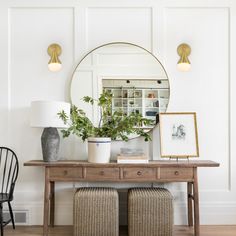 a wooden table with two chairs and a mirror on the wall above it in a white room