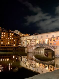 a bridge over a body of water at night with buildings in the background and lights on