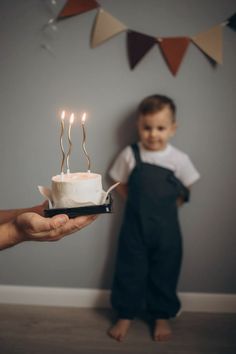 a small child standing next to a cake with candles on it and someone holding the cake in front of him