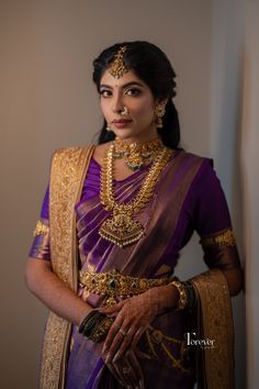 a woman in a purple and gold sari is posing for the camera with her hands on her hips