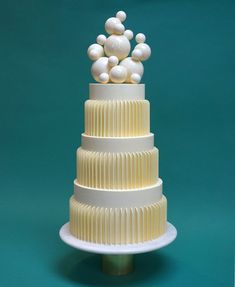 a three tiered cake with white icing and balls on top, against a teal background