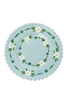 a blue plate with white flowers and green leaves on the rim, against a white background