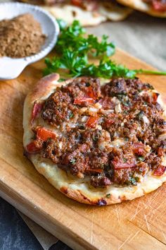 a pizza sitting on top of a wooden cutting board next to a bowl of seasoning