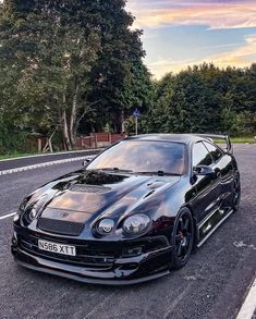 a black sports car parked on the side of the road with trees in the background