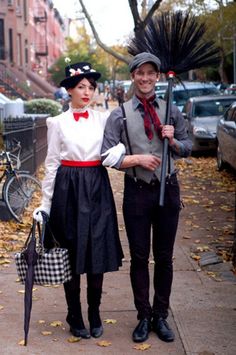 a man and woman dressed in costumes standing next to each other on a sidewalk with umbrellas