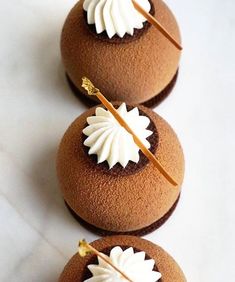 three chocolate desserts with white frosting and gold decoration on top, sitting on a marble surface