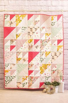 a quilt hanging on a brick wall next to a potted plant and white vase