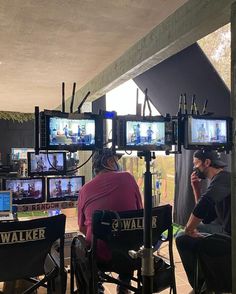 two men sitting in front of televisions on top of wooden chairs and talking on the phone