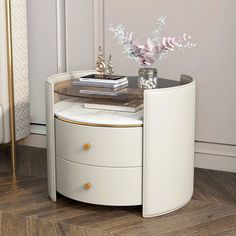 a white round table with two drawers and a vase on the top, next to a chair