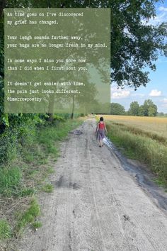 a person walking down a dirt road next to a field with trees and grass in the background