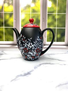 a black tea pot sitting on top of a white counter next to a windowsill