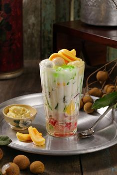 a glass filled with fruit on top of a metal tray next to nuts and leaves