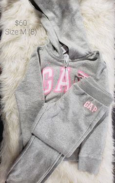 a gray hoodie with pink letters on the front and bottom is laying on a fluffy white rug