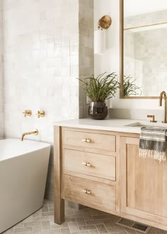 a white bath tub sitting next to a wooden sink vanity under a large framed mirror