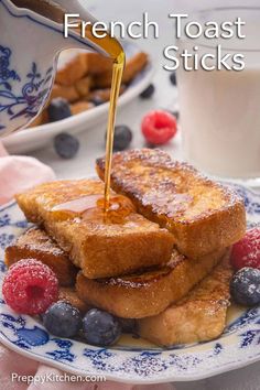 french toast sticks on a plate with berries and syrup being drizzled over them