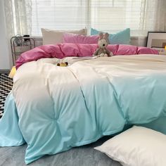 a bed with pink and blue sheets, pillows and a stuffed animal on top of it