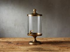 a glass jar with a gold faucet on top sitting on a wooden table