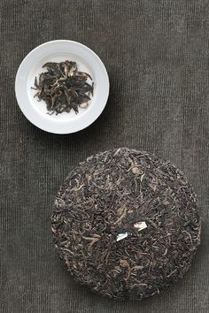 a white bowl filled with black tea next to a plate full of green tea leaves