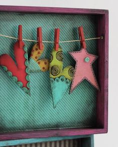 three felt stars hanging from clothes pins on a string in a purple box with pink and green trim