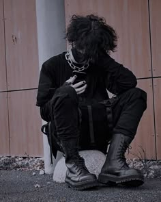 a man sitting on top of a rock next to a tall pole wearing black boots