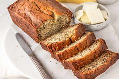 sliced loaf of banana bread on a plate next to butter and two bowls with bananas