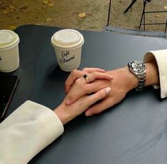 two people holding hands with coffee cups in the background