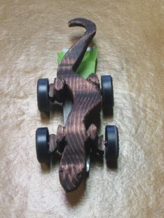 a wooden toy car sitting on top of a brown carpeted floor next to a green piece of paper