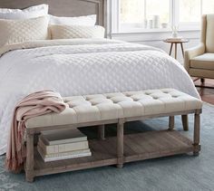 the bed is made with white linens and has a bench underneath it for storage