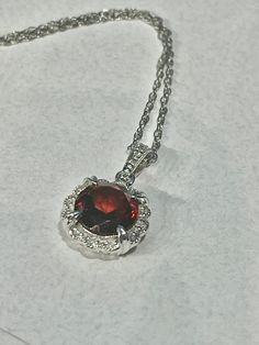 14K White Gold Diamond & Garnet scalloped Halo fancy pendant. This Halo pendant features a beautiful faceted 2.18ct round 8mm red Garnet stone, surrounded by diamonds, 0.05ctw. the chain is a 14K white gold rope chain, 1mm, 18" longThe arrangement of its facets is similar to that of a round brilliant, designed to maximize light and color. The sides are fancy scroll work with an open back. The stone is set in a 14K white gold prong setting which has an attractive halo design and holds the garnet Exquisite Red Jewelry With Gemstone Accents, Elegant Ruby Round Pendant Jewelry, Brilliant Cut Ruby Necklace In Round Shape, Elegant Red Diamond Gemstones, Ruby Round Necklace With Prong Setting, Ruby Necklace With Brilliant Cut, Exquisite Round Ruby Necklaces, Ruby Necklace With Prong Setting, Fine Ruby Round Pendant Jewelry