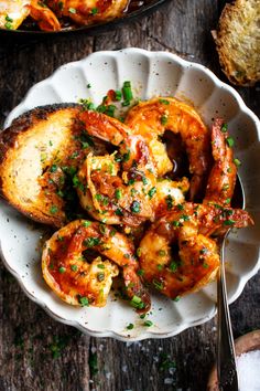 a bowl filled with shrimp and bread on top of a wooden table next to a fork