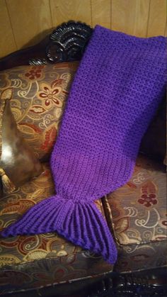 a purple knitted mermaid tail sitting on top of a couch next to a pillow