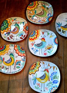 four plates with birds painted on them sitting on a wooden table