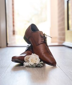 a pair of brown shoes sitting on top of a wooden floor next to a white flower