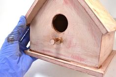 a person in blue gloves holding a wooden birdhouse