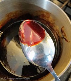 a spoon filled with sauce sitting on top of a pot full of dirt and water