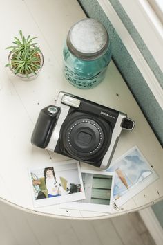 an old camera sitting on top of a table next to pictures and a potted plant