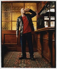 a man standing in front of a bar drinking from a glass with his hand on his head