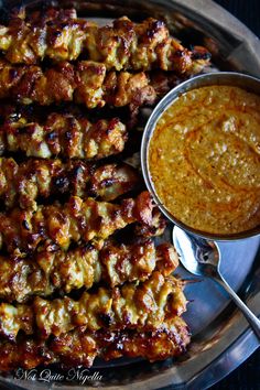 several skewers of food on a silver platter with a bowl of dipping sauce