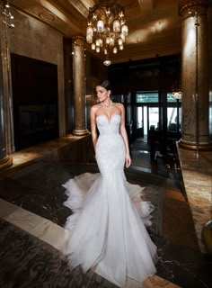 a woman in a white wedding dress standing in a room with chandeliers on the ceiling