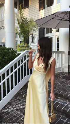 a woman in a yellow dress is drinking from a white cup and holding an umbrella